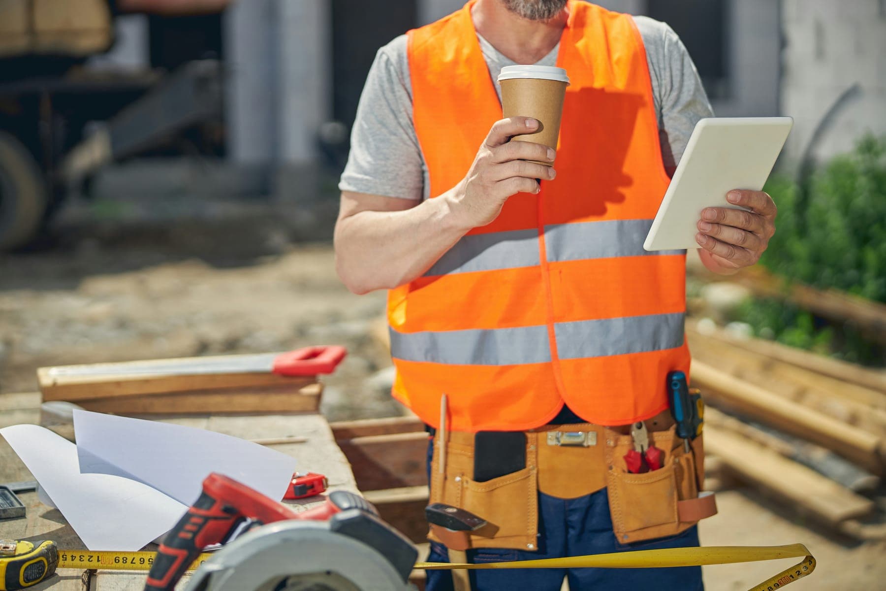 Worker with a coffee reading a tablet on a building site
